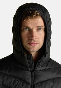 Čierna izolovaná páperová bunda s vysokým golierom a kapucňou, s prešívanou textúrou a predným zipsovým zapínaním.