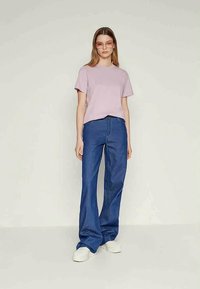T-shirt de manga curta lilás claro combinado com jeans azul de boca de sino e ténis brancos. O conjunto apresenta um corte descontraído e uma textura suave.