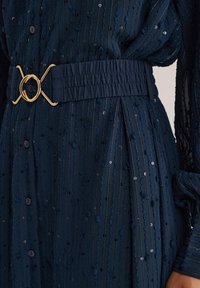 Navy Kleid mit Paillettenverzierungen, das aus einem strukturierten Stoff gefertigt ist, über eine Knopfverschluss verfügt und einen breiten elastischen Bund mit einer goldenen runden Schnalle hat.
