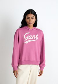 Pink hoodie with a loose design, featuring a white logo and text “Gant” on the front. Soft fabric, kangaroo pocket, and hood.