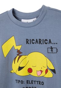 Blauses Baumwoll-T-Shirt mit einem großen gelben Pikachu-Graphic, das mit roten Wangen entspannt, über dem Text ist ein Blitzsymbol und ein Batteriensymbol.