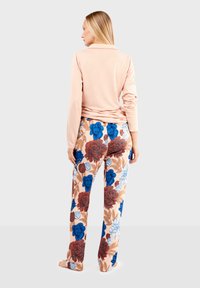 Haut rose clair à manches longues associé à un pantalon fleuri orné de grandes fleurs bleues et rouges sur fond pastel ; coupe décontractée et matériau doux.