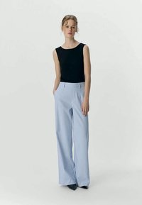 Top negro sin mangas combinado con pantalones de tiro alto y pierna ancha a rayas azules y blancas. Textura suave y ajuste entallado con bolsillos.