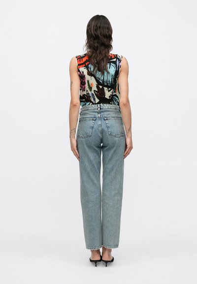Πολύχρωμο αμάνικο τοπ με αφηρημένο ανθικό σχέδιο, συνδυασμένο με ανοιχτόχρωμο τζιν ψηλόμεσο παντελόνι με ίσια ποδάρια και μαύρα τακούνια.