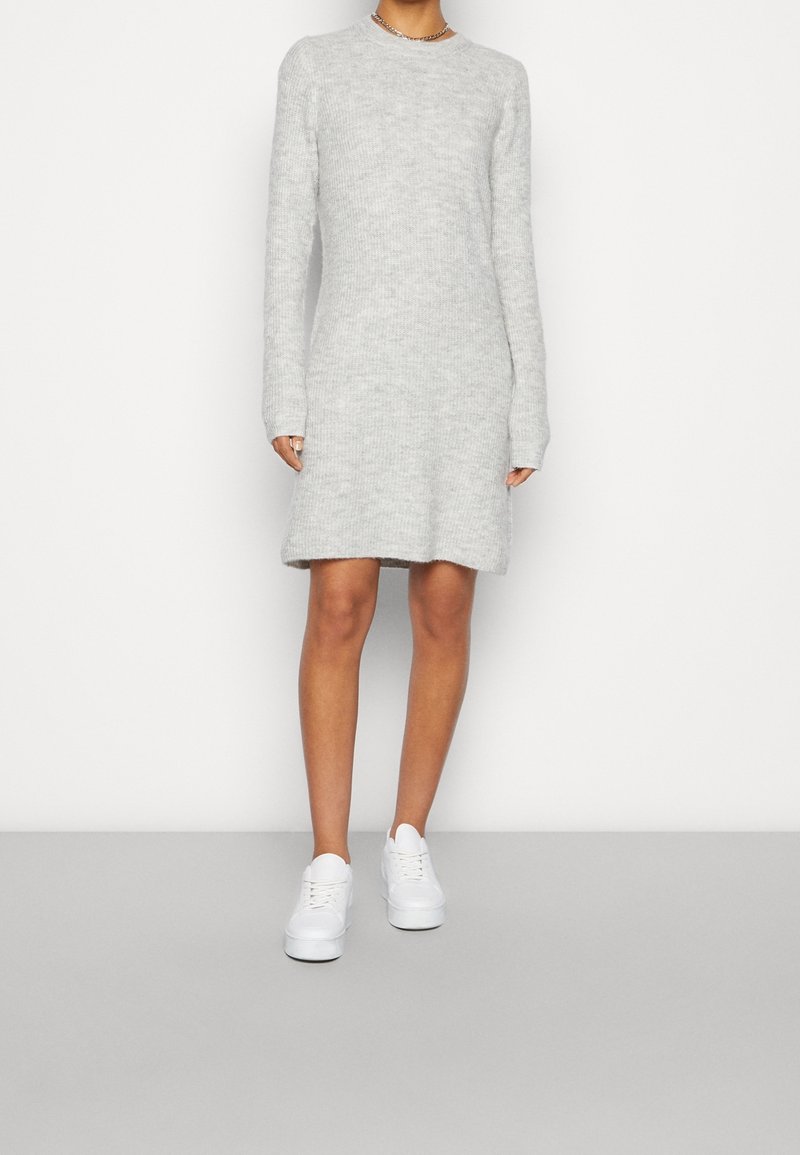 Vestito grigio a maglia con maniche lunghe, scollo rotondo e orlo a metà coscia, abbinato a sneaker bianche. Texture morbida e vestibilità comoda.