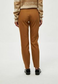 Pantaloni marroni su misura con vestibilità dritta, caratterizzati da un design minimalista e una texture liscia. Abbinati a scarpe nere.