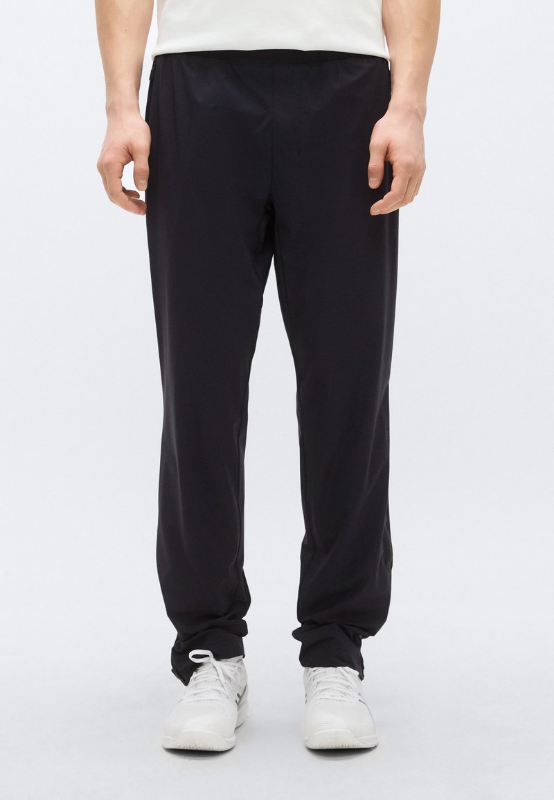 Fekete, könnyű nadrág gumis derékrésszel, szűkített fazonban és sima tapintású anyagból. Fehér sportcipővel párosítva.