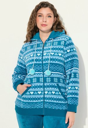 Teal zip-up huppari pehmeästä fleece-materiaalista, jossa on monimutkaiset lumihiutale- ja sydänten kuviot, sekä kaksi pom-ponia vetoketjujen päässä ja taskuissa.
