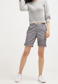 Pantalones cortos de algodón gris con un ajuste relajado, puños doblados y bolsillos laterales, combinados con un suéter texturizado gris claro y zapatillas blancas.