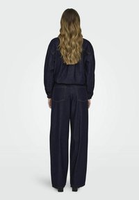 Conjunto de chaqueta de denim y pantalones de pierna ancha en un lavado oscuro. Incluye un ajuste relajado, mangas largas y detalles de costura en contraste.