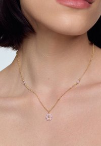 Złoty naszyjnik z różowym wisiorkiem w kształcie kwiatu z trzema płatkami i kamieniem w środku, ozdobiony małymi różowymi koralikami wzdłuż łańcuszka.