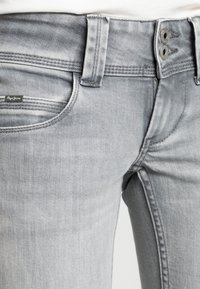 Grå jeans i denim med en figursydd design, tvåknappsknäppning och en logotagg på framfickan. Slät textur med minimal blekning.