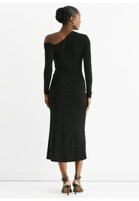 Black, one-shoulder dress with long sleeves, fitted silhouette, accented with white polka dots and a midi length, worn with strappy heels.