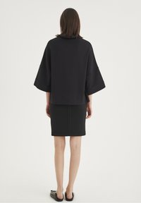 Černý oversize top s širokými rukávy, spárovaný s přiléhavou černou sukní. Hladký materiál s čistým designem, z pohledu zezadu.