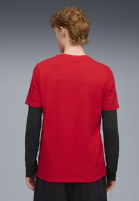 Rød kortærmet t-shirt med rund halsudskæring, lavet af glat stof, lagdelt over en sort langærmet skjorte, med et ensfarvet rygdesign.