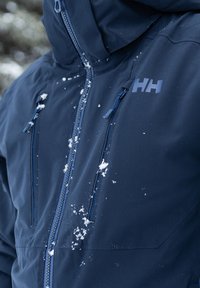 Námořnická voděodolná bunda se zapínáním na zip, dvěma hrudními kapsami a logem. Sněhové vločky na povrchu naznačují venkovní použití.