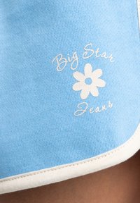 Světle modrá látka s bílými detaily, na které je bílý potisk textu "Big Star Jeans" a jednoduchá květinová grafika uprostřed.