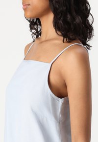 Ανοιχτό μπλε αμάνικο τοπ με λεπτές τιράντες, τετράγωνη λαιμόκοψη και μαλακό, ελαφρώς υφαντό ύφασμα. Ορατή λεπτομέρεια στη ραφή πλευράς.