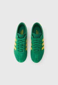 Πράσινα σουέντ αθλητικά παπούτσια με κίτρινες ρίγες, υφή στο μπροστινό μέρος και επίπεδα κορδόνια. Διαθέτουν επενδεδυμένη εσωτερική σόλα και λαστιχένια εξωτερική σόλα.