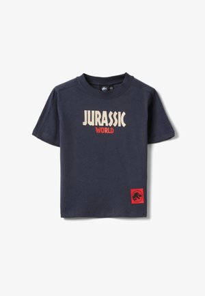 T-shirt à manches courtes bleu marine avec le texte "Jurassic World" en beige et rouge, et un patch rouge avec un logo de dinosaure en bas.