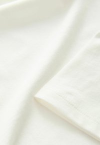 Vitt bomullstyg draperat med en slät textur. Har en mjuk finish och subtila sömmar nära fållen.