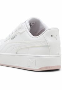 Baskets blanches avec tige en cuir, col rembourré et semelle en caoutchouc rose. Présente un logo Puma en argent et des accents texturés sur les côtés.