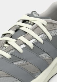 Pilkas sportinis batas su tekstūruotu viršumi, lygiomis detalėmis, baltomis batų raišteliais ir subtiliu tinklo akcentu šonuose.