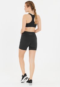 Mustapohjainen urheilutoppi ja yhteensopivat shortsit, joissa on korkea vyötärö, sivutaskut ja sileä, venyvä kangas.