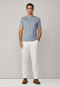 Šedé tričko s krátkým rukávem z jemné látky, spárované s bílými kalhotami. Hnědé kožené boty dotvářejí outfit. Jednoduchý, ležérní design.