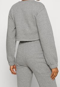 Felpa cropped grigia chiara in morbido tessuto testurizzato, con maniche ampie e polsini elasticizzati. Design semplice con scollo rotondo e orlo pulito.