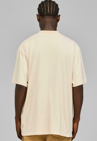 Kortermet, beige t-skjorte laget av myk bomull. Har en avslappet passform og rund hals. Ingen synlige logoer eller mønstre.