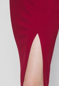 Gros plan d'une jupe rouge avec une fente à l'avant dévoilant la peau nue sur un fond gris clair.