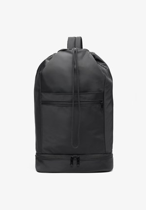 Black nylon backpack with a rounded shape, featuring a front zipper pocket, adjustable straps, and a smooth texture. Double zipper at the bottom.