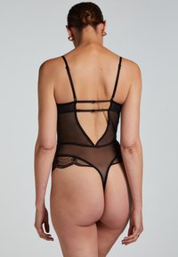 Body din plasă neagră prezintă bretele ajustabile, un decolteu adânc la spate și accente din dantelă de-a lungul marginilor, punând în evidență un design transparent și delicat.