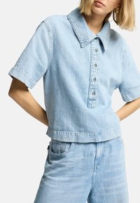Lys blå denim skjorte med korte ærmer og stor krave, fem knaplukninger og en cropped kant, med en glat tekstur.