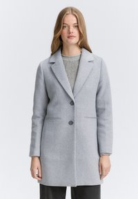 Lichtgrijze wollen jas met een notch lapel, twee knopen aan de voorkant en zijzakken; gladde textuur met een getailleerde pasvorm en minimale details.