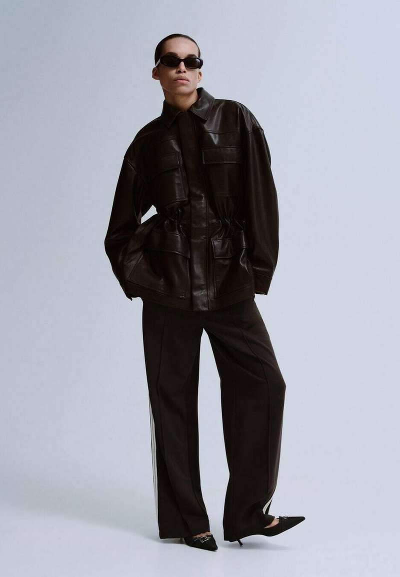 Sort læderjakke med indsnævret talje, to forlommer og krave, kombineret med sorte bukser med vide ben og spidse sko.