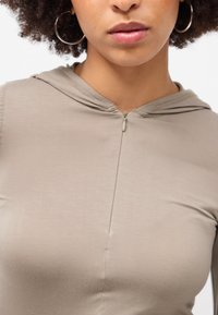 Lysebrune zip-up hoodie med en tætsiddende design, der har en blød, glat tekstur, en hætte og en central sømdetalje.