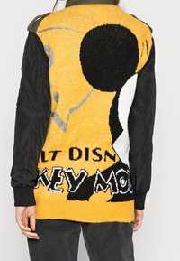 Knit sweater with a yellow front, featuring a large Mickey Mouse graphic, black sleeves, and "WALT DISNEY" text in contrasting colors.
