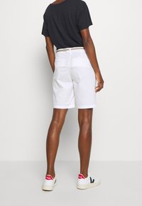Hvide bomuldsshorts med en afslappet pasform, suppleret med et vævet bælte. Blandet med en sort kortærmet skjorte og hvide sneakers.