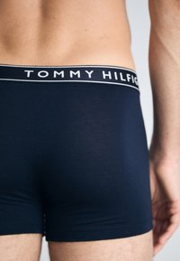 Marineblå boxershorts laget av elastisk stoff med en kontrasterende hvit "TOMMY HILFIGER" logo-linning. Glatt tekstur og tettsittende design.