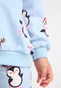 Blue sweatshirt with penguin prints, featuring ribbed cuffs and soft texture. Coordinating patterned pants visible; playful winter theme.