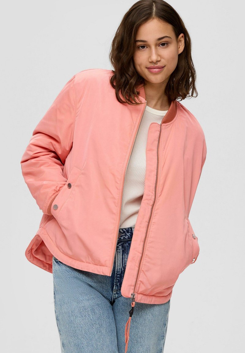 Chaqueta bomber rosa con cierre frontal, cuello redondo, bolsillos laterales y puños elásticos, combinada con jeans azules. Textura de tela suave.