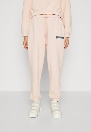 Lyse rosa joggebukser laget av myk stoff, med elastisk midje og snor samt en liten farget logo på låret.