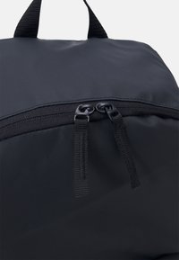 Musta kangaskassi, jossa on vetoketju kaksipuolisilla metallivetimillä ja teksturoiduilla kahvoilla paremman otteen saamiseksi. Tasainen pinta ja minimalistinen muotoilu.