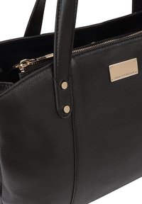 Zwarte leren handtas met een gladde textuur, goudkleurige hardware, twee stevige handvaten en een rits aan de bovenkant; heeft een merkembleem aan de zijkant.