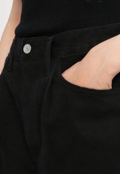 Jean noir taille haute, avec une fermeture à bouton argenté, des poches latérales et une texture lisse. Coutures visibles le long des coutures.
