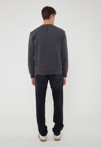 Felpa grigia scura con maniche lunghe, polsini e orlo a costine, con un piccolo dettaglio vicino al collo. Abbinata a pantaloni in denim scuri e sneakers.