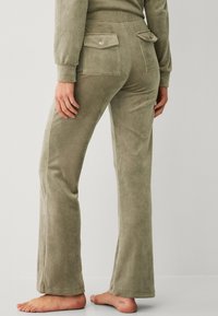 Olivengroene fluwelen flared broek met twee achterzakken en een gladde textuur. Geen zichtbare hardware. Model draagt ze blootsvoets.