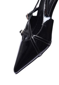 Scarpa nera in vernice con tacco alto, punta affusolata, caratterizzata da cinturini incrociati e un design elegante con una finitura lucida.